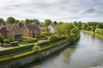 Homes set back from a calm river behind a flood-defence wall